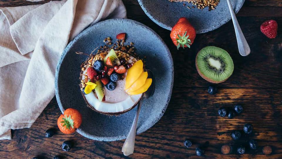 Fruchtige Frühstücks Bowl mit knusprigem Buchweizen-Granola, angerichtet in Kokosnusshälften.