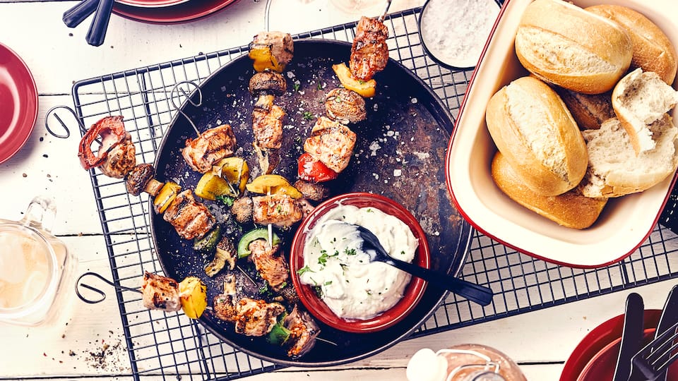 Mediterraner Genuss für Ihre nächste Grillparty: Pikant gewürzte Fleischspieße, dazu Zaziki und Baguette Brötchen.